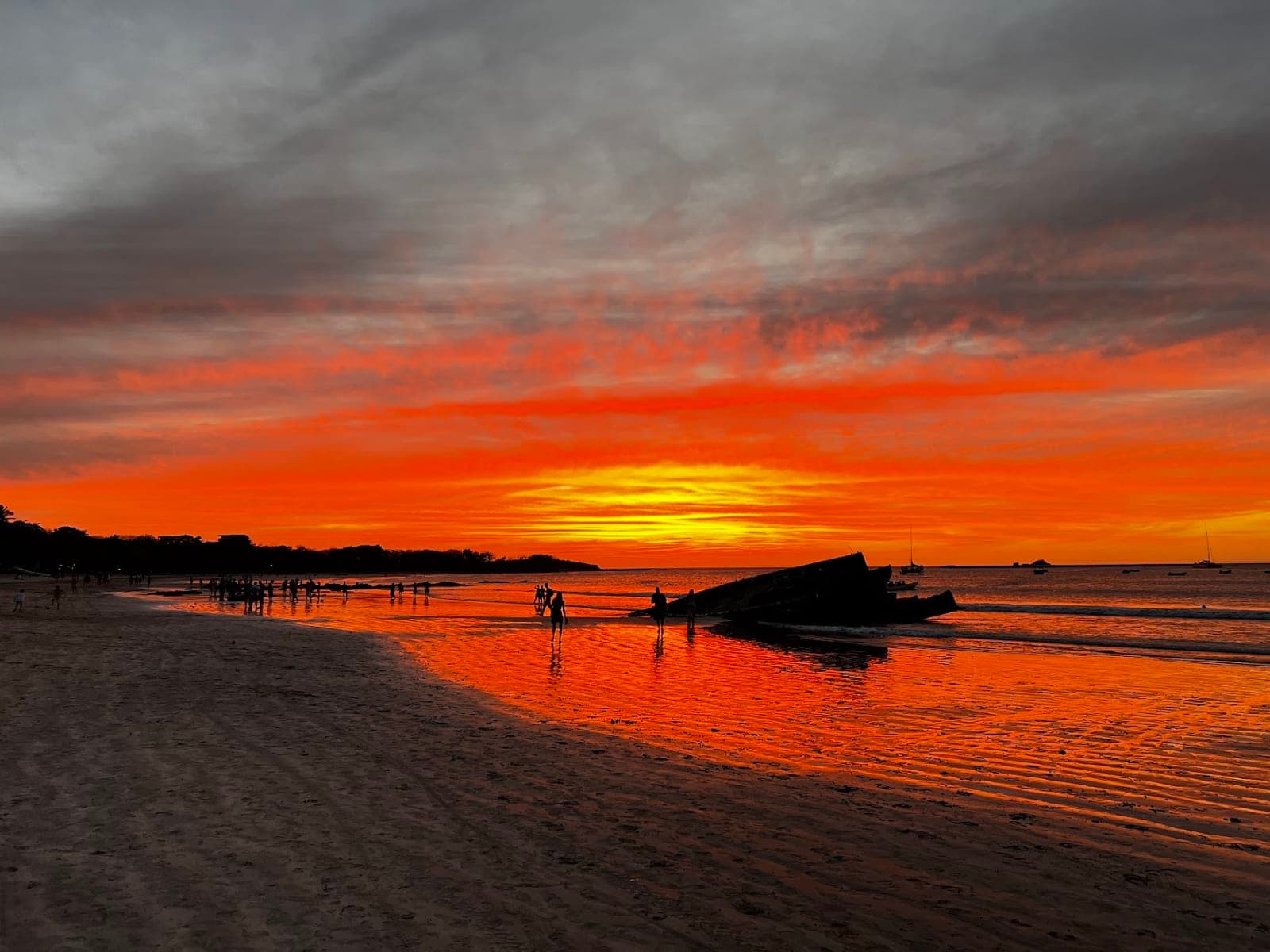 An orange sunset over a beach with people silhouetted on the sand
